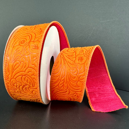 A partially unrolled roll of 1.5X10Y Orange Fuchsia Double Sided Embossed Dupioni Ribbon features intricate floral patterns against a dark backdrop. This elegant wired ribbon has a contrasting pink reverse, adding sophistication.